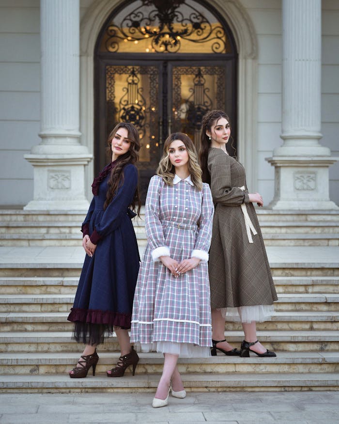 Three women in vintage dresses pose gracefully on manor steps. Beautiful and elegant fashion portrait.