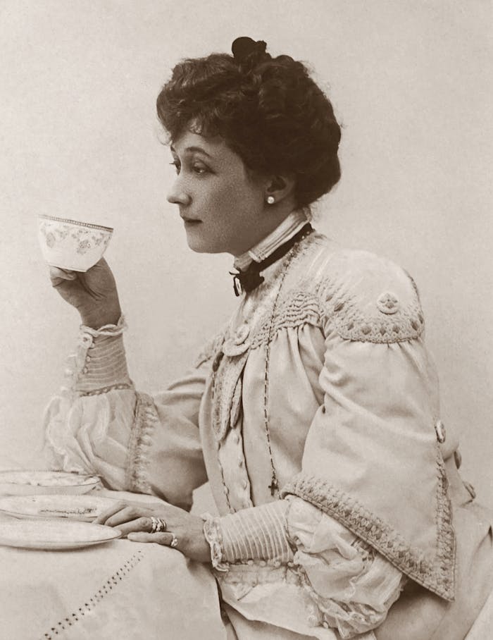 Elegant Victorian woman sipping tea in a vintage sepia-toned portrait.